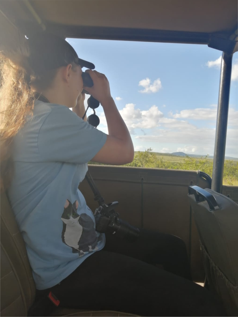 Janelle, face of Eatventurer, looking through binoculars during a game drive